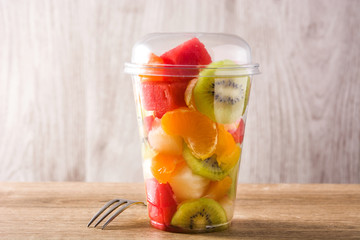 Fresh cut fruit in a plastic cup on wooden table
