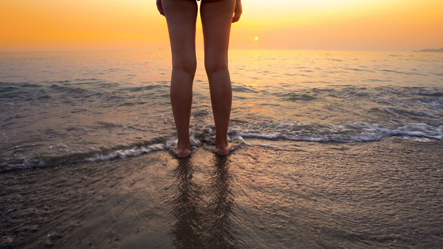 Woman feet splashed by sea waves on beach sunset. Calm serene relaxing scene of ocean water splashing on feet on beautiful beach