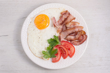 Taste fried eggs with fried bacon, tomatoes and greens on a white wooden table. The idea for an American-style breakfast recipe. Beautiful serving, serving dishes in the cafe. Top view