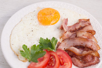 Taste fried eggs with fried bacon, tomatoes and greens on a white wooden table. The idea for an American-style breakfast recipe. Beautiful serving, serving dishes in the cafe. Close-up top view