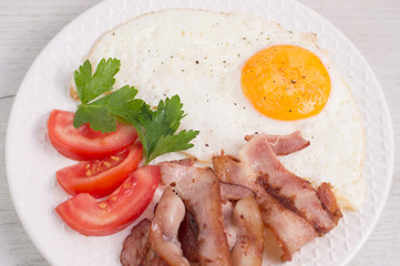 Taste fried eggs with fried bacon, tomatoes and greens on a white wooden table. The idea for an American-style breakfast recipe. Beautiful serving, serving dishes in the cafe. Close-up top view
