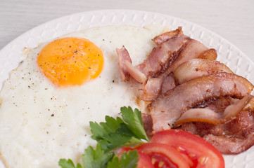 Taste fried eggs with fried bacon, tomatoes and greens on a white wooden table. The idea for an American-style breakfast recipe. Beautiful serving, serving dishes in the cafe. Close-up top view