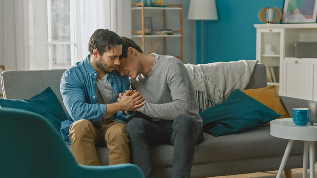 Sad Queer Drama Concept. Boyfriend Is Unhappy And Depressed About Something. His Gay Friend Is Comforting Him, Holding His Hands. Miserable Man Puts His Head On A Shoulder And Cries.