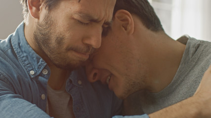 Fototapeta premium Sad Queer Drama Concept. Close-up Shot of a Unhappy and Depressed Boyfriend. His Gay Friend is Comforting Him, Holding His Hands. Miserable Man Puts His Head on a Shoulder and Cries.