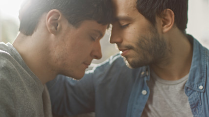 Cute Male Queer Couple Put Their Heads Together and Close Their Eyes. Sweet Gentle Loving Gay Relationship Moment. Room Has Modern Interior.