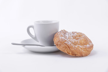 A cup of hot coffee and a roll of puff pastry with powdered sugar on top