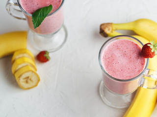 Strawberry smoothie with banana in glasses on white table