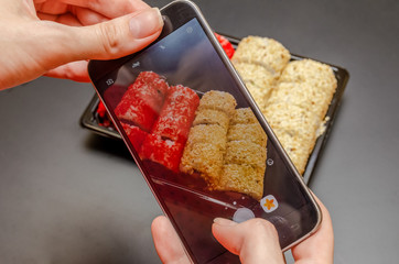 A girl photographs red and white sushi on the phone from different angles. Photo close up.