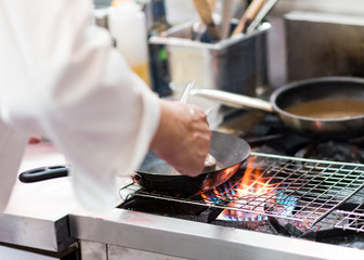 Chef cooking with flame in a frying pan on a kitchen stove.