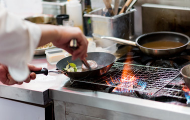 Chef cooking with flame in a frying pan on a kitchen stove.