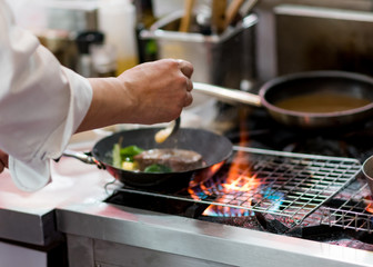 Chef cooking with flame in a frying pan on a kitchen stove.