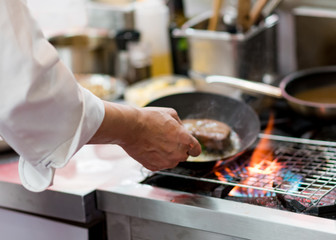 Chef cooking with flame in a frying pan on a kitchen stove.