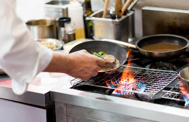 Chef cooking with flame in a frying pan on a kitchen stove.