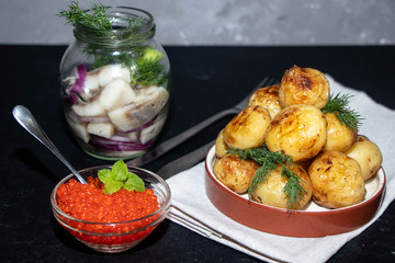 Boiled and roasted young potatoes, red caviar in a transparent scallop, herring sliced.