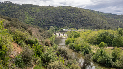 Eine historische Dampflok überquert im Hintergrund auf einer alten Bogenbrücke ein Flusstal in...