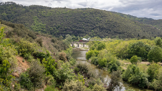 Eine historische Dampflok &uuml;berquert im Hintergrund auf einer alten Bogenbr&uuml;cke ein Flusstal in den Cevennen