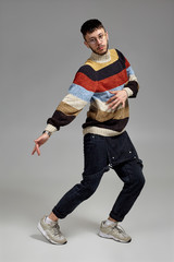 Full-length portrait of a funny guy dancing in studio on a gray background.