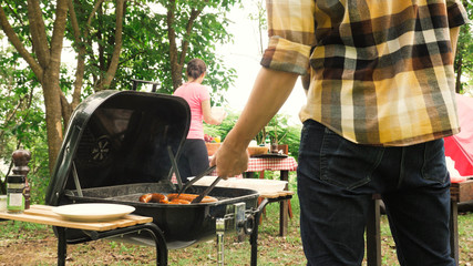 People praparing barbecue party with bbq stove roasting sausage and prepare table in garden