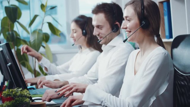 Close up view of happy young operators of call center with headset fool around at their workplace, the female worker turns to camera, smiles and gives thumb up. Positive emotions, good mood