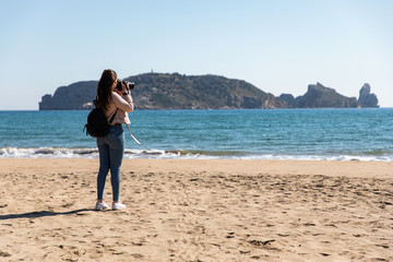 Back view of woman taking pictures with DSLR camera of islands from the beach - Medes Islands