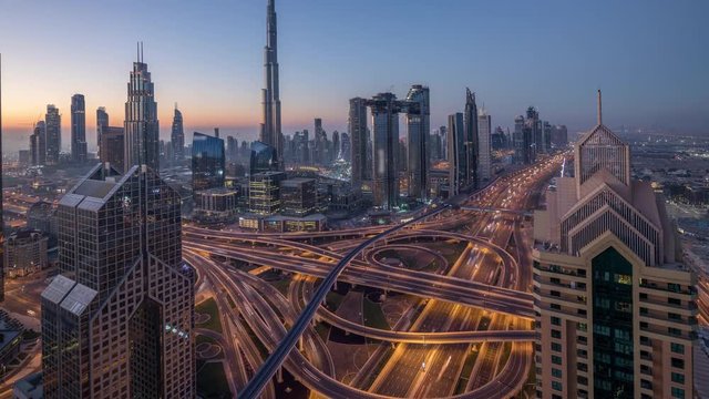 Dubai downtown skyline with tallest skyscrapers and busiest traffic on highway intersection night to day transition timelapse. Aerial view from above