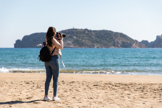 Back view of woman taking pictures with DSLR camera of islands from the beach - Medes Islands