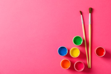 Flat lay composition with gouache and paint brushes on pink background, space for text