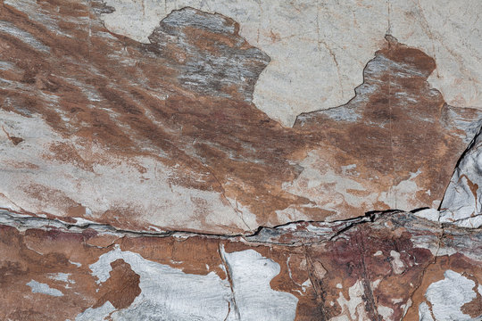 Textura de rocha natural que lasca em camadas e forma um desenho abstrato de tonalidades de cinzento a castanho avermelhado com uma v&aacute;rias rachas das quais uma mais prenunciada na horizontal.