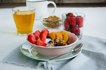 Healthy vegetarian breakfast. A bowl of granola, berries and fruit. In the background a glass of green tea and strawberries on a white background. The concept of healthy eating, diet
