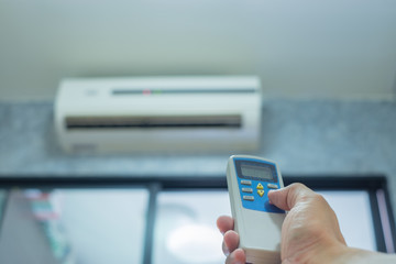 Hand holding remote control. Adjusting temperature of of air conditioner mounted on a white wall.