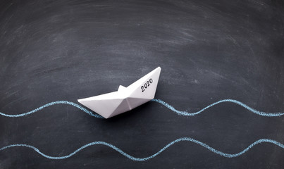 White paper boat with 2020 concept on black board background