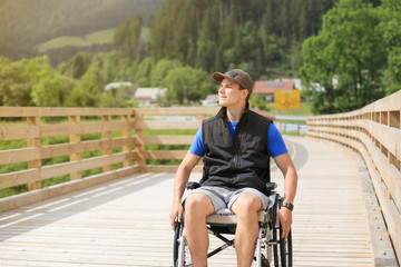 Disabled young man on a wheelchair on a wooden bridge path enjoying in nature looking at beautiful view