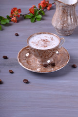 Coffee with milky foam topped with cinnamon in a cup against the gray wooden background