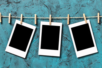 Three blank vintage polaroid instant photograph frame with empty isolated space hanging on rope on blue textured background. Copy and paste your photo
