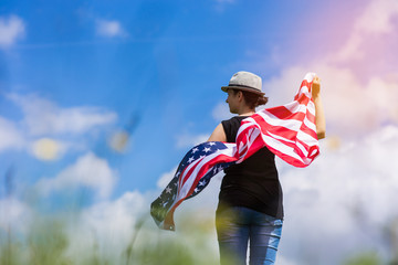 Woman holding the american flag outdoors on a meadow.  4th of July - Independence day.