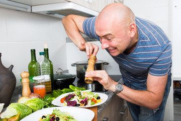male prepares two salads and fills them with pepper