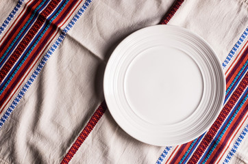 Empty white plate on a napkin on an old wooden brown background, top view. Image with copy space. Kitchen table with a towel and a plate - top view with copy space. 