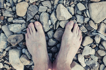 barefoot male legs on the river stones
