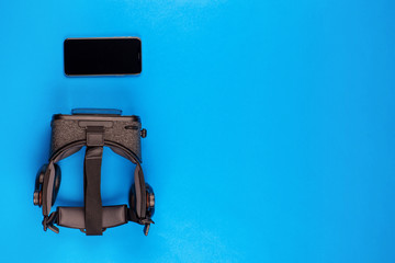 Phone and a vr set on blue background, shot from above, aligned to the left.