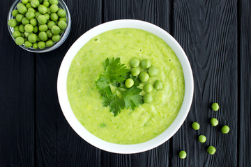 Pea soup  in the white bowl on the black wooden background.Top view.