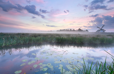 Dutch windmill by lake in misty sunrise