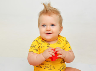 Funny chubby 9 month old kid with hairdo in yellow clothes sitting on white background with toys