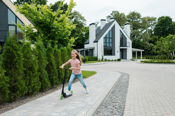 happy kid smiling while riding scooter near trees on street © LIGHTFIELD STUDIOS