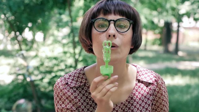 Young woman in glasses blowing bubbles outdoors in the park	