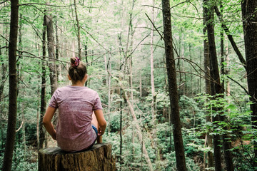 Teen Teen Girl Sitting on a Stump Looking Out into a green Forest full of trees