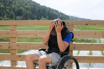 Disabled young man on a wheelchair in nature feeling depressed, lonely and sad