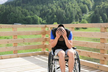 Disabled young man on a wheelchair in nature feeling depressed, lonely and sad