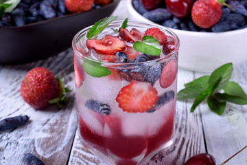 Lemonade with cherries, honeysuckles, strawberries, red syrup and ice in a glass topped with mint 