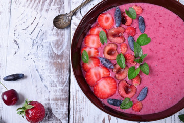 Berry smoothie bowl topped with strawberries, cherries, honeysuckles and mint