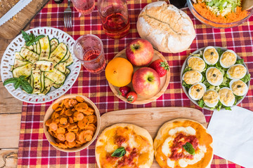 Red checkered tablecloth on wooden panel. Mix of vegetables, salad end eggs ready for the brunch. Italian pizza on chopping board. Natural light